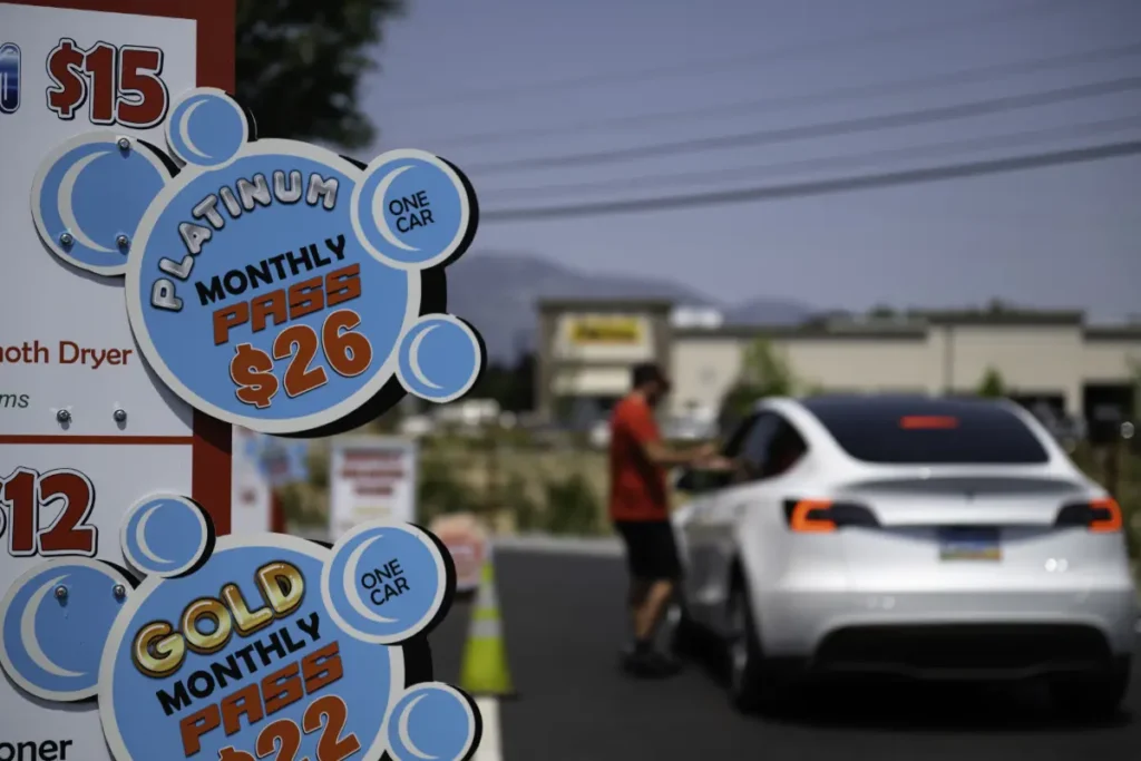 red barn car wash sign monthly unlimited pricing with staff member and white tesla in the background