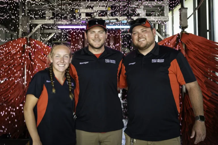 red barn car wash staff in front of the entrance to the tunnel car wash with car wash brushes in the background