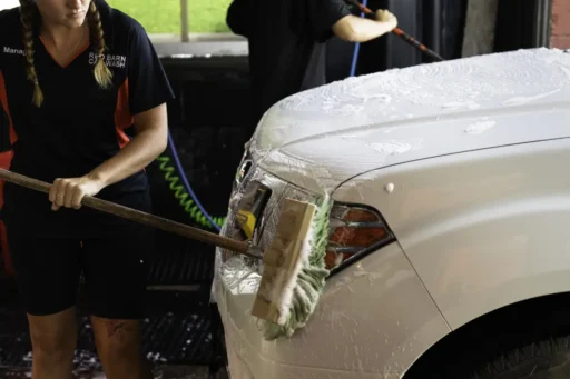 red barn car wash prewash prep scrub brushing the front bumper, grill, and headlights of a white nissan frontier